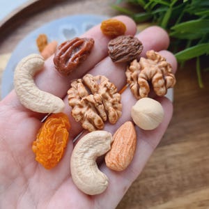 May include: A variety of nuts and dried fruit, including cashews, walnuts, almonds, and apricots. The nuts and fruit are arranged on a hand.