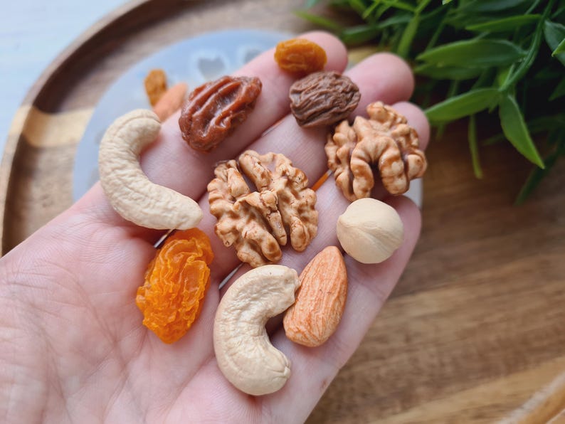 May include: A variety of nuts and dried fruit, including cashews, walnuts, almonds, and apricots. The nuts and fruit are arranged on a hand.