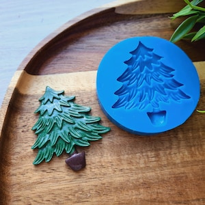 Può includere: Uno stampo in silicone blu per realizzare decorazioni per l'albero di Natale. Lo stampo è mostrato con un ornamento per l'albero di Natale in plastica verde che è stato realizzato usando lo stampo.