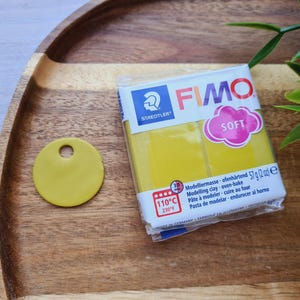 May include: A package of yellow FIMO Soft modeling clay. The package has a blue and white label with the brand name and instructions for baking the clay. The clay is oven-bake and can be used for crafting and sculpting.
