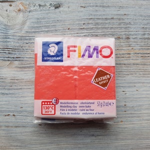 Könnte beinhalten: Eine rote Packung FIMO Modelliermasse mit Ledereffekt. Die Packung ist mit dem Markennamen, der Art der Masse und der Backtemperatur von 130°C oder 265°F beschriftet. Die Packung enthält auch das Gewicht der Masse, 57 g (2 oz).