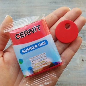 May include: A red package of CERNIT Number One polymer clay. The package has text in multiple languages, including "Pâte polymère opaque", "Opaque polymer clay", "Opake Polymermasse", "Pasta Polimerica opaca", and "Arcilla polimerica opaco".