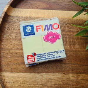 May include: A package of FIMO Soft modeling clay, a light yellow color with a blue and white logo. The package says "Modellermasse ofenhärtend 57g (2oz) e" and "110°C 230°F".