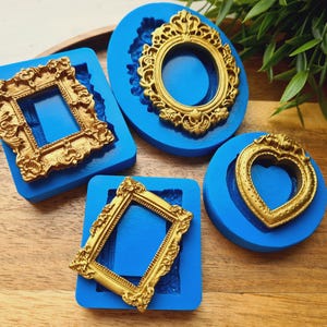 May include: Four blue silicone moulds for casting, each featuring a different ornate gold-coloured frame design. The shapes include a rectangular frame, an oval frame, a heart-shaped frame, and a smaller rectangular frame with intricate detailing.
