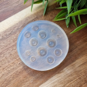 K&ouml;nnte beinhalten: Eine transparente Silikonform mit 10 runden Vertiefungen in verschiedenen Gr&ouml;&szlig;en. Die Form befindet sich auf einer Holzoberfl&auml;che.