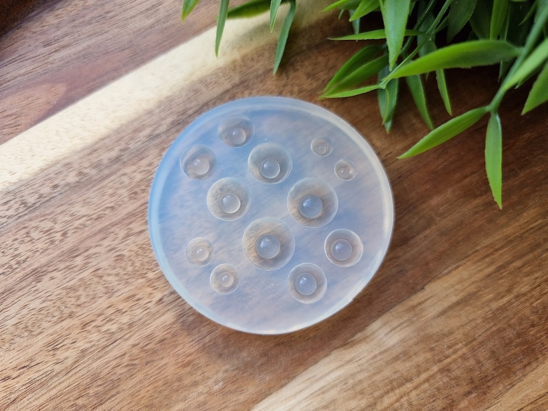 K&ouml;nnte beinhalten: Eine transparente Silikonform mit 10 runden Vertiefungen in verschiedenen Gr&ouml;&szlig;en. Die Form befindet sich auf einer Holzoberfl&auml;che.