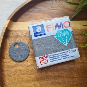 May include: A package of gray FIMO Effect modeling clay with a diamond-shaped logo. The package includes instructions for baking the clay at 110 degrees Celsius or 230 degrees Fahrenheit.