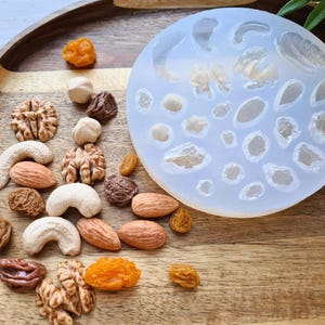 May include: A silicone mold with various shapes of nuts and seeds. The mold is on a wooden tray with a variety of nuts and seeds scattered around it.