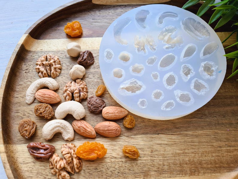 May include: A silicone mold with various shapes of nuts and seeds. The mold is on a wooden tray with a variety of nuts and seeds scattered around it.