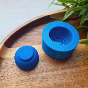 Puede incluir: Dos moldes de silicona azul para hacer velas o jabón. Los moldes están sobre una superficie de madera.
