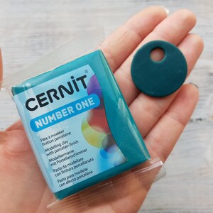 May include: A teal blue block of polymer clay in a clear plastic package. The package has the text "CERNIT NUMBER ONE" printed on it. The text is in black and white. The clay is for modeling and has a porcelain finish.
