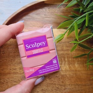 May include: A package of pink Sculpey Souffl&eacute; polymer clay. The package has a purple and pink label with the brand name and product details. The clay weighs 1.7 oz (48 g).