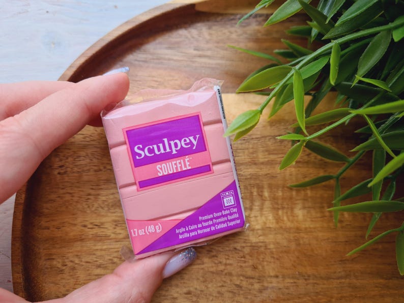 May include: A package of pink Sculpey Souffl&eacute; polymer clay. The package has a purple and pink label with the brand name and product details. The clay weighs 1.7 oz (48 g).