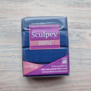 Könnte beinhalten: Ein blauer Block Sculpey Souffle Back-Knete mit einem rosa Etikett, auf dem "Sculpey Souffle" und "1.7 oz (48.2 g)" steht. Das Etikett trägt auch den Text "Premium Oven-Bake Clay" in Englisch, Französisch und Spanisch.