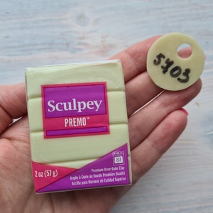Könnte beinhalten: Ein 2 Unzen (57 Gramm) Block Sculpey Premo Backofen-Modelliermasse in hellgrüner Farbe. Die Verpackung hat ein rosa-weißes Etikett mit dem Markennamen und Produktinformationen. Ein weißes Etikett mit der Nummer 5703 ist im Hintergrund sichtbar.