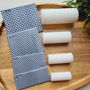 May include: A wooden tray holds several items. There are three gray, square, textured mats and four white, cylindrical objects with a textured surface. Green leaves are in the background.