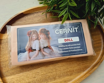 May include: A rectangular block of Cernit Doll modelling clay with a porcelain finish, encased in clear plastic packaging. The label features a photograph of two children and the text Cernit Doll, Modelling clay with porcelain finish.