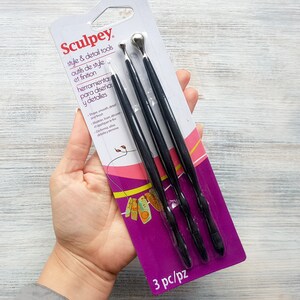 Puede incluir: Un paquete de tres herramientas de estilo y detalle Sculpey negras. El paquete es morado y rosa con el texto "Sculpey", "style & detail tools", "outils de style et finition", "herramienta para dise&ntilde;a y detalles", y "3 pc/pz".