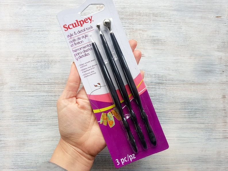 Puede incluir: Un paquete de tres herramientas de estilo y detalle Sculpey negras. El paquete es morado y rosa con el texto "Sculpey", "style & detail tools", "outils de style et finition", "herramienta para dise&ntilde;a y detalles", y "3 pc/pz".