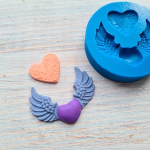 Peut inclure: Un moule en silicone bleu avec deux ailes en forme de cœur et un cœur au centre. Il y a deux ailes en forme de cœur finies avec un cœur violet au centre et un seul cœur orange avec les mots "Je t'aime" dessus.