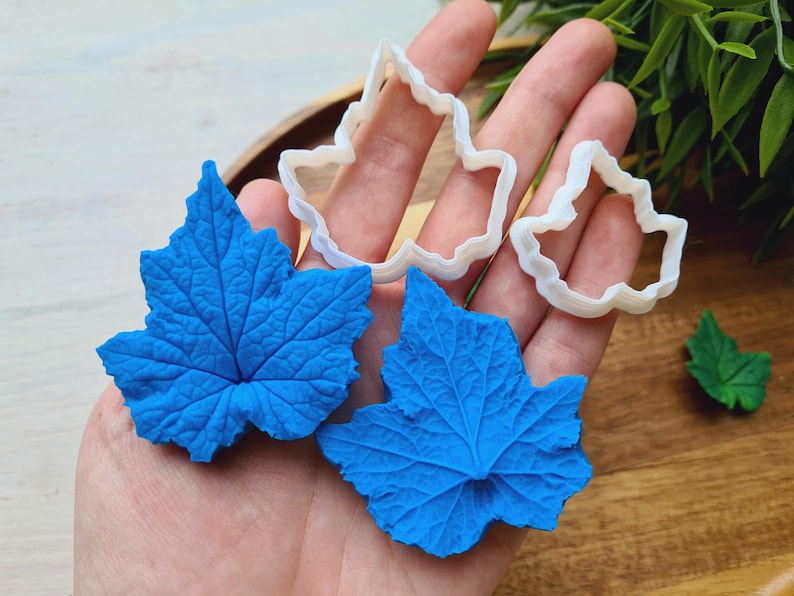 Puede incluir: Dos formas de hojas azules de fondant hechas con cortadores de galletas con forma de hoja. Los cortadores son de pl&aacute;stico blanco y se muestran en la imagen.