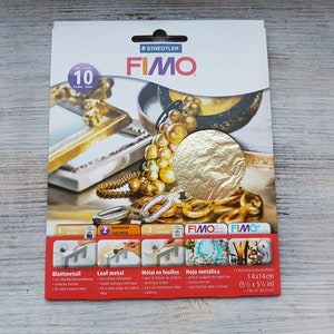 Puede incluir: Un paquete de 10 hojas de oro para usar con arcilla polimérica Fimo. El paquete muestra un primer plano de una hoja de oro y una variedad de joyas de oro. El paquete está etiquetado como "Fimo Leaf Metal" y "14x14cm (5 1/2 x 5 1/2 in)".