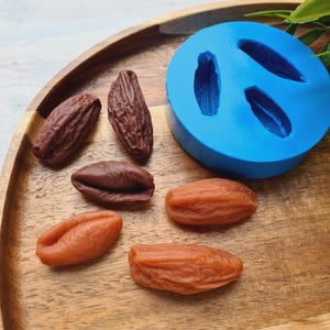 May include: A blue silicone mold with three cavities shaped like dates. Six dates, three brown and three orange, are on a wooden tray.