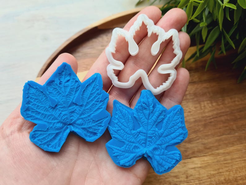 May include: Two blue silicone molds of grape leaves, one with a detailed texture and the other with a smooth surface. A white plastic mold of a grape leaf is also shown.