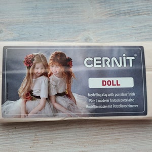 May include: A package of Cernit Doll modeling clay with a porcelain finish. The label features two girls with flowers in their hair. The package also includes the text "Modelling clay with porcelain finish".