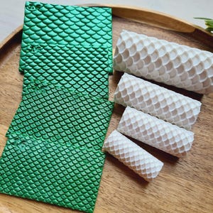 May include: A wooden tray holds green, textured squares and white, cylindrical objects. The green squares have a scale-like pattern. The white cylinders, of varying sizes, also feature a scale-like design. The items are arranged on a wooden tray.