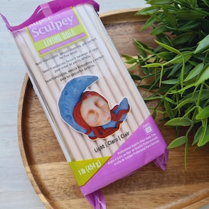 May include: A package of Sculpey Living Doll polymer clay in light color. The package features a sleeping doll illustration and the text "Semi-translucent, smooth blending, and perfect for fine details".