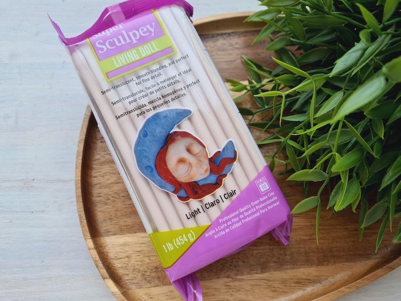 May include: A package of Sculpey Living Doll polymer clay in light color. The package features a sleeping doll illustration and the text "Semi-translucent, smooth blending, and perfect for fine details".