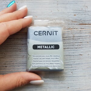 Puede incluir: Un paquete de arcilla polim&eacute;rica met&aacute;lica de la marca Cernit. El paquete es plateado y tiene el texto "CERNIT METALLIC" impreso en &eacute;l. El texto "P&acirc;te polym&egrave;re avec micas effet m&eacute;tallique Polymer clay with metallic mica's effect Polymermasse mit Glimmer-Metalleffekt Pasta polimerica con mica effetto metallico Arcilla polimerica met&aacute;lica con efecto mica" est&aacute; impreso en el paquete en varios idiomas.