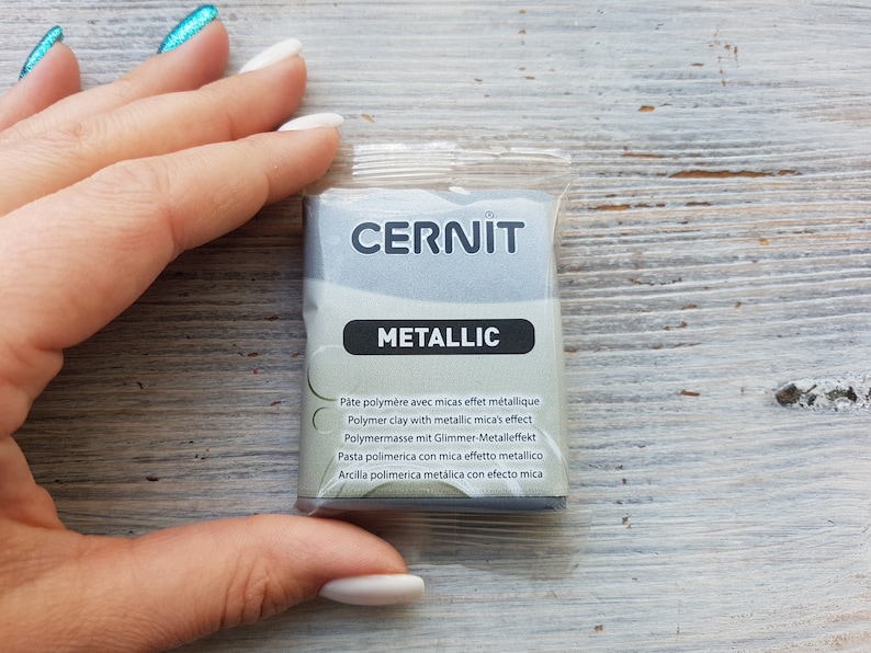 Puede incluir: Un paquete de arcilla polim&eacute;rica met&aacute;lica de la marca Cernit. El paquete es plateado y tiene el texto "CERNIT METALLIC" impreso en &eacute;l. El texto "P&acirc;te polym&egrave;re avec micas effet m&eacute;tallique Polymer clay with metallic mica's effect Polymermasse mit Glimmer-Metalleffekt Pasta polimerica con mica effetto metallico Arcilla polimerica met&aacute;lica con efecto mica" est&aacute; impreso en el paquete en varios idiomas.