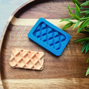 May include: A blue silicone mold shaped like a waffle, on a wooden tray with a waffle made from the mold.