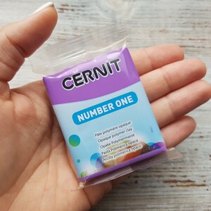 May include: A purple and blue package of CERNIT Number One opaque polymer clay. The package has text in multiple languages.