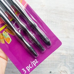 Puede incluir: Un paquete de tres herramientas de metal negro con puntas redondeadas. El paquete es morado y tiene el texto "3 pc/pz" impreso en la parte inferior.