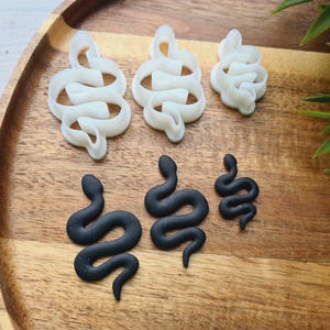 Può includere: Cinque stampini per biscotti a forma di serpente, tre bianchi e due neri. Gli stampini bianchi sono a forma di spirale, mentre gli stampini neri hanno una forma più lineare.