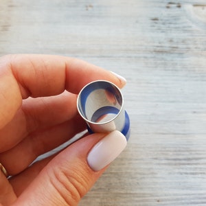 May include: A silver and blue metal cookie cutter in the shape of a circle.