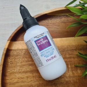 May include: A clear bottle of Liquid Sculpey brand liquid polymer clay. The bottle is labeled "Clear | Transparent | Transparente" and "2 fl oz (59 ml)".