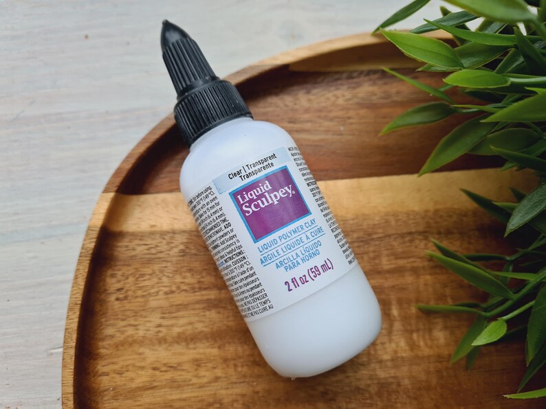 May include: A clear bottle of Liquid Sculpey brand liquid polymer clay. The bottle is labeled "Clear | Transparent | Transparente" and "2 fl oz (59 ml)".