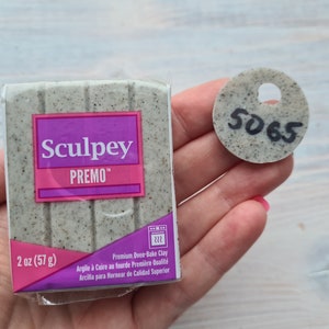 Puede incluir: Un paquete de arcilla polimérica Sculpey Premo, 57 g, en color gris moteado. También se ve una pequeña muestra redonda de arcilla gris moteada con el número "5065".