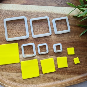 Op de afbeelding: Een set van 10 vierkante koekjesvormen van wit plastic in verschillende maten, getoond op een houten oppervlak met vierkante fondantvormen in geel die met de vormen zijn uitgesneden.