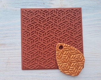 Pode incluir: Um tapete de silicone vermelho para assar com um padrão geométrico de folhas sobrepostas. Um tapete de silicone menor, de cor dourada, com o mesmo padrão é colocado sobre o tapete maior.