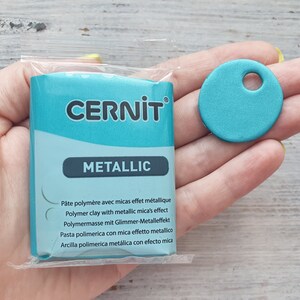 May include: A package of turquoise blue polymer clay with the brand name "CERNIT" and the word "METALLIC" printed on the front. The package also includes text in French, German, Italian, Spanish, and English describing the product as polymer clay with metallic mica.
