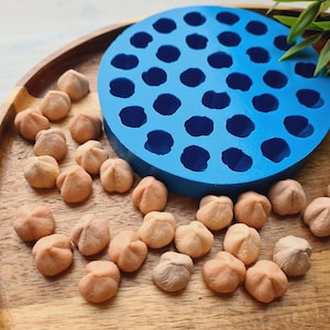 Puede incluir: Un molde de silicona azul con 36 cavidades redondas, sentado en una bandeja de madera con numerosos objetos pequeños, de color marrón claro e irregulares.