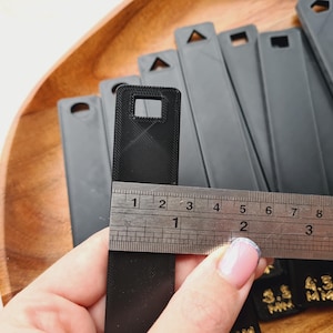 Peut inclure: Collection d'objets rectangulaires noirs avec des trous de diff&eacute;rentes formes en haut. Une r&egrave;gle est plac&eacute;e sur l'un des objets, indiquant une mesure d'environ 10 cm. Les objets sont sur une surface en bois.