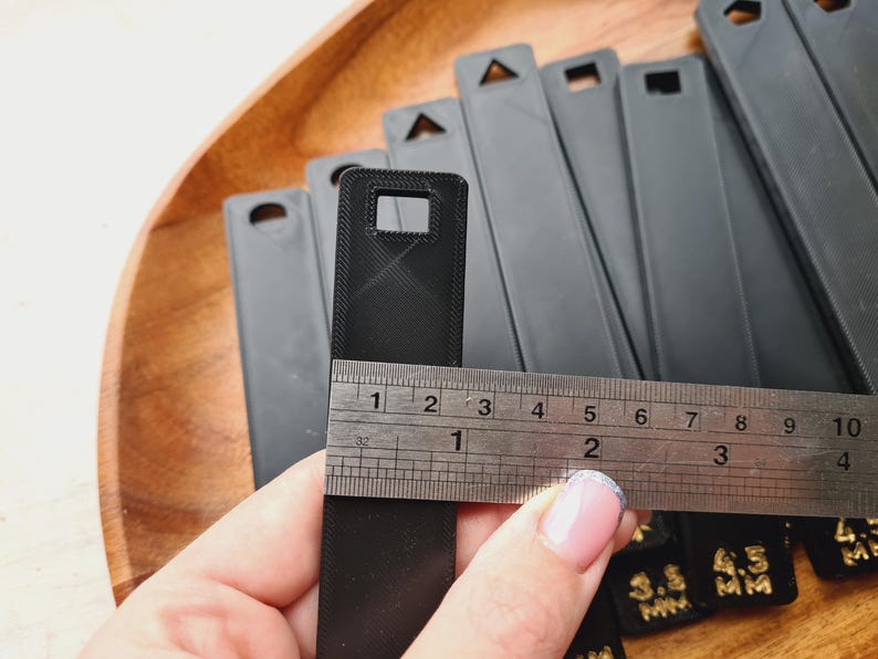 Peut inclure: Collection d'objets rectangulaires noirs avec des trous de diff&eacute;rentes formes en haut. Une r&egrave;gle est plac&eacute;e sur l'un des objets, indiquant une mesure d'environ 10 cm. Les objets sont sur une surface en bois.