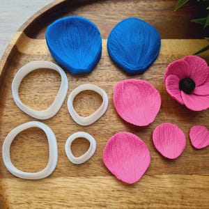 Puede incluir: Un conjunto de moldes de silicona para hacer decoraciones con forma de flor. El conjunto incluye moldes para pétalos, hojas y una pieza central. Los moldes están sobre una superficie de madera.