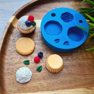 Puede incluir: Un molde de silicona azul con seis formas diferentes para hacer cupcakes en miniatura, junto con un cupcake en miniatura, una base de cupcake en miniatura y otros suministros de repostería en miniatura.